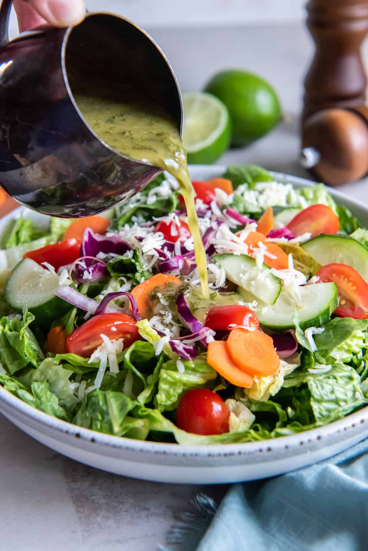 A hand pouring cilantro lime vinaigrette on to a colorful salad.