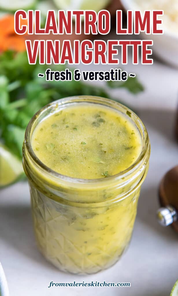 A mason jar filled with cilantro lime vinaigrette with cilantro and vegetables behind it with text.