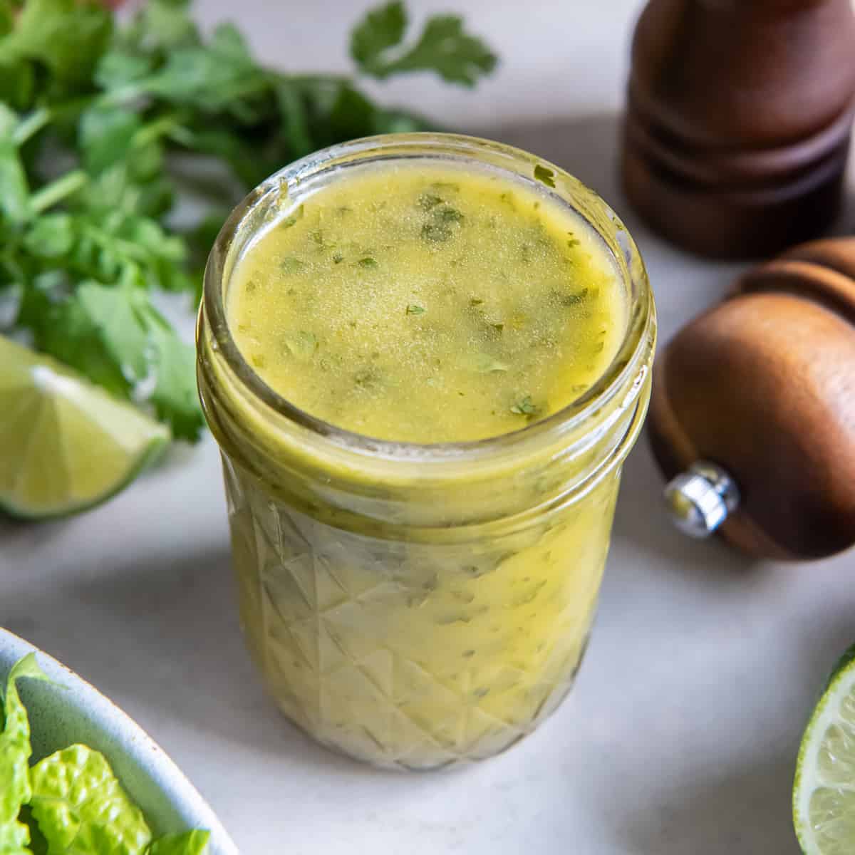 A mason jar filled with cilantro lime vinaigrette with cilantro behind it.