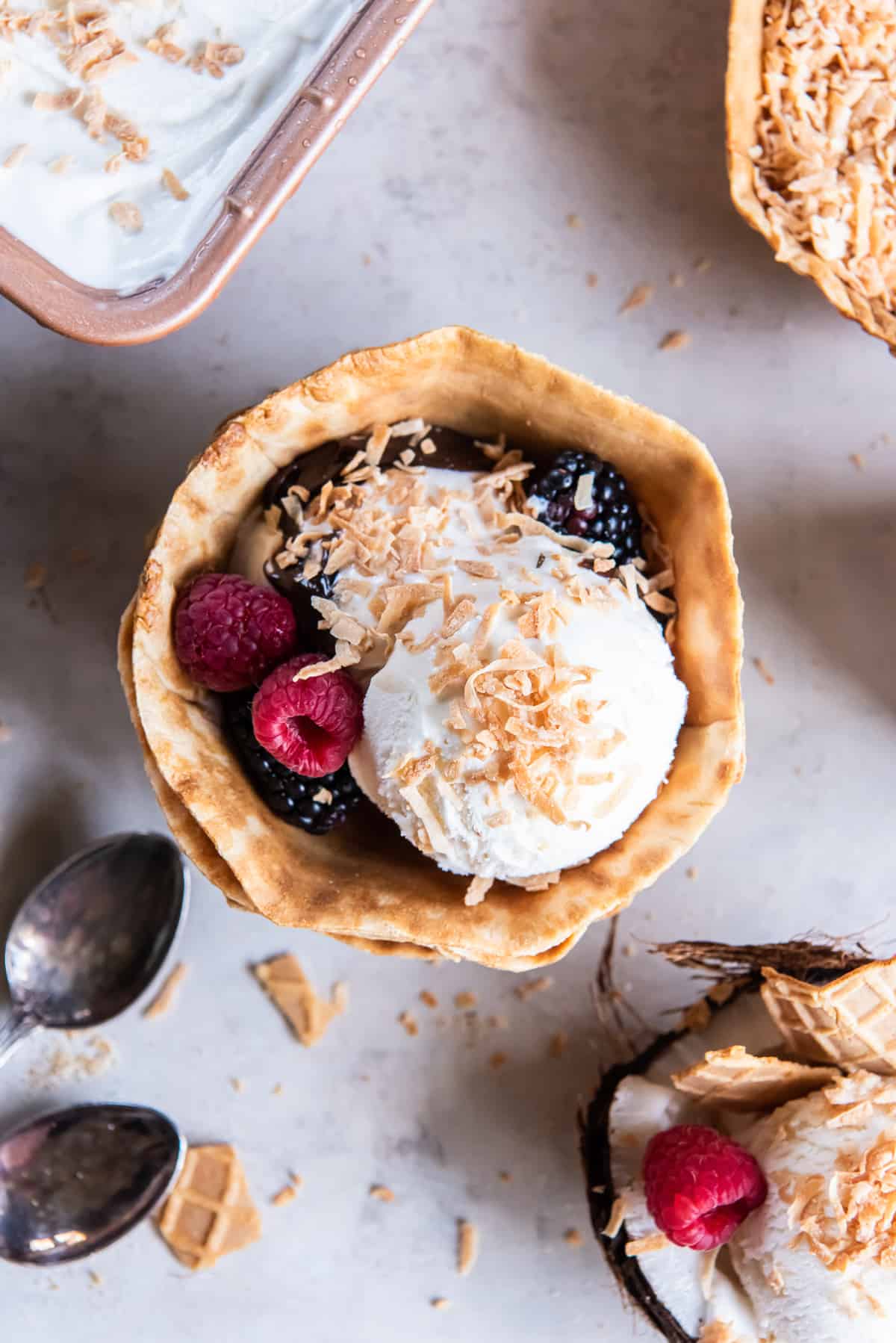 A top down shot of coconut ice cream in a waffle cone cup topped with toasted coconut and fresh berries.