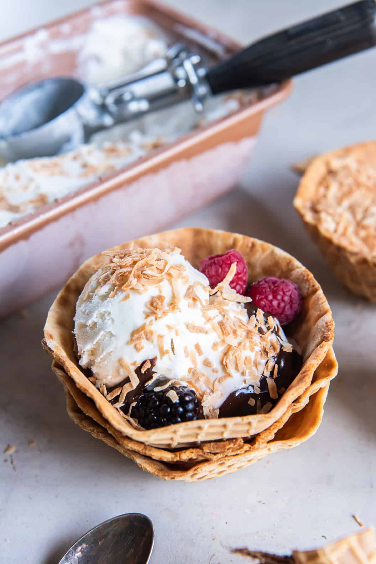 A stack of two waffle cone cups filled with coconut ice cream with toasted coconut and berries.