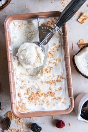 A top down shot of an ice cream scoop resting in a metal loaf pan filled with coconut ice cream.
