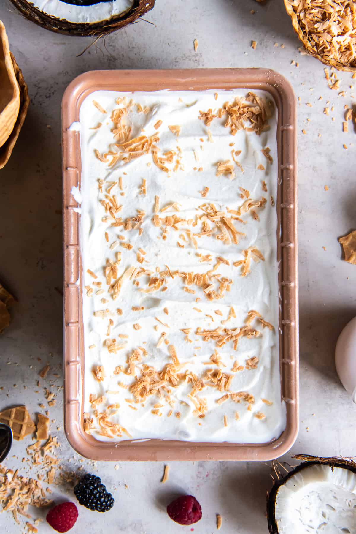 A top down shot of coconut ice cream topped with toasted coconut in a metal loaf pan.