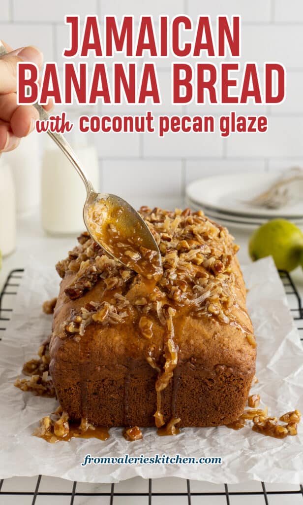 A hand drizzling a coconut pecan mixture from a spoon over a loaf of banana bread.