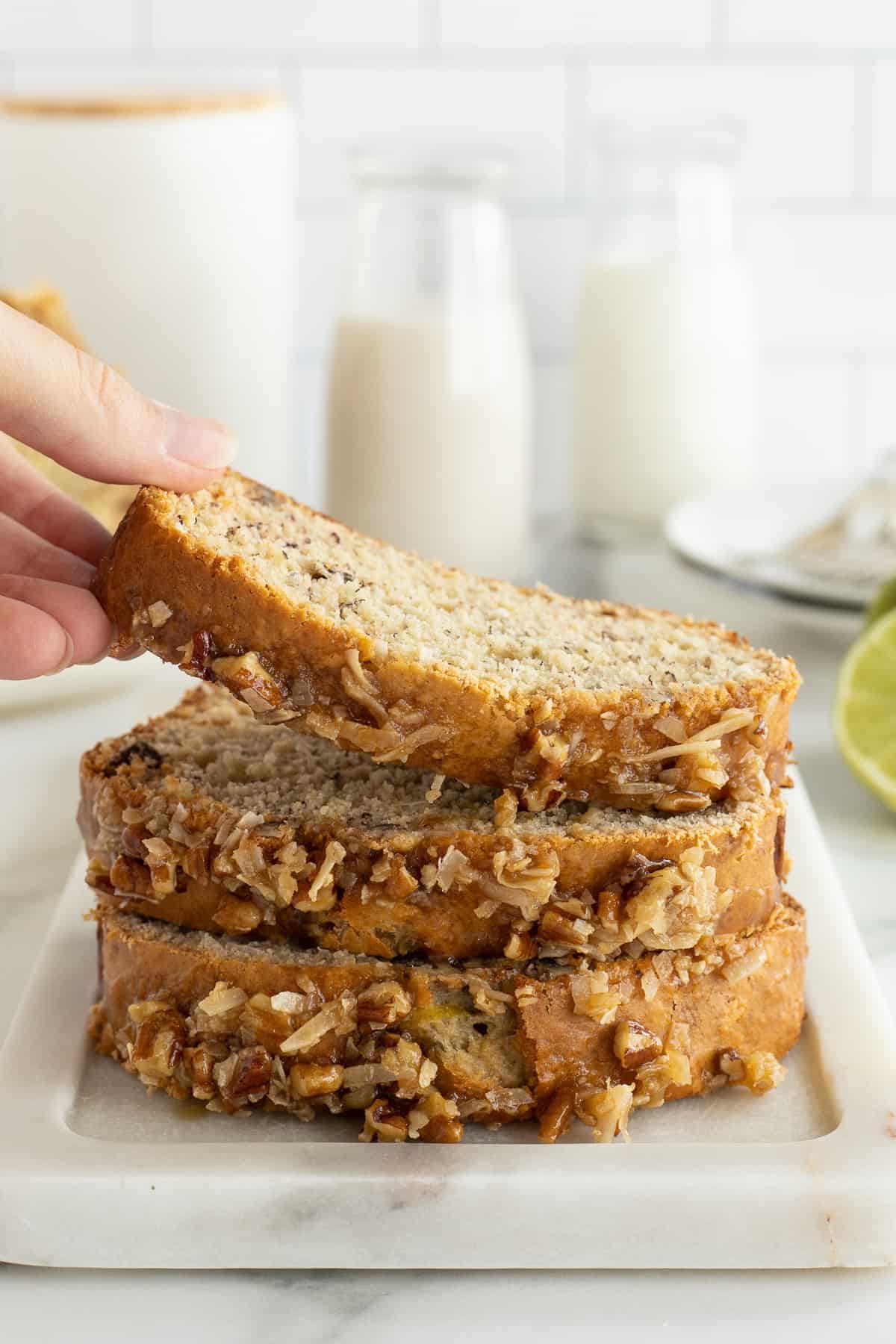 A hand lifting a slice of Jamaican Banana Bread off of a stack of three slices.