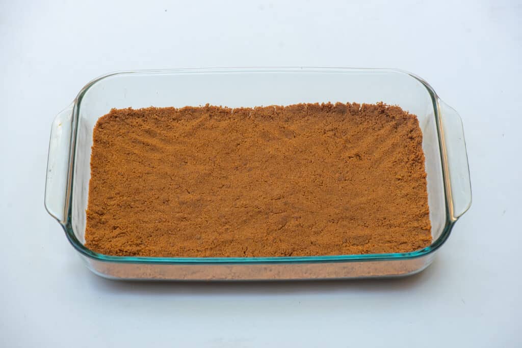 A gingersnap crust spread across the bottom of a glass baking dish.