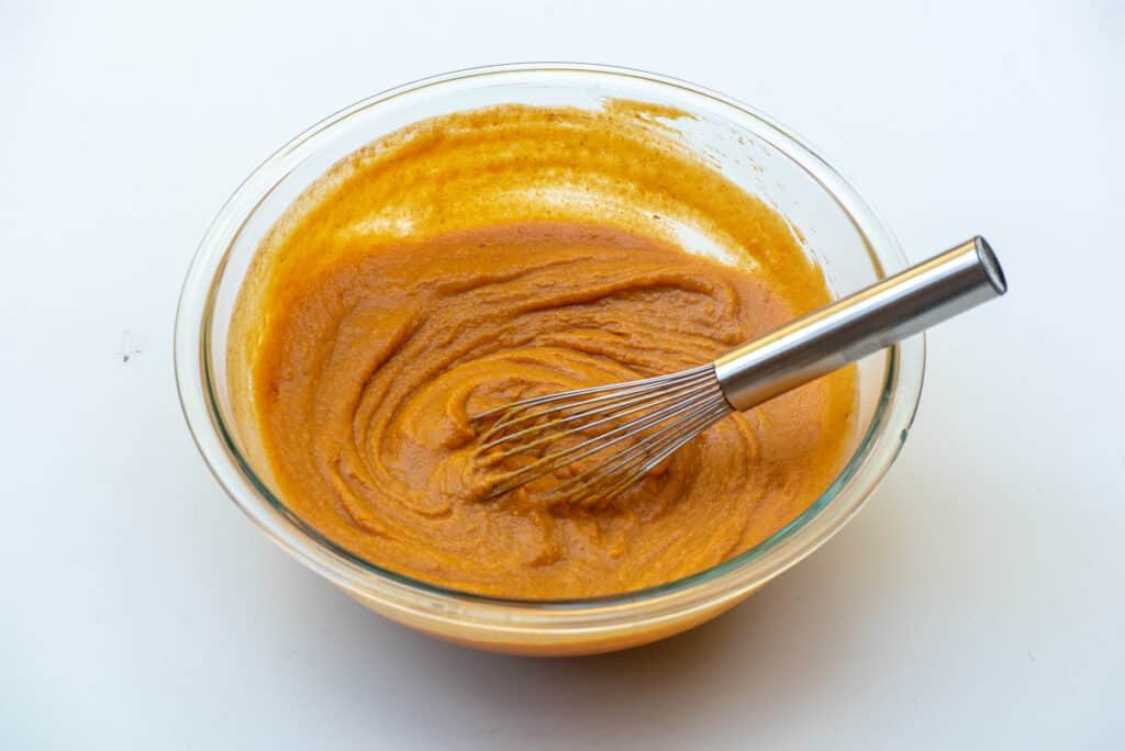 A whisk resting in a bowl with a creamy pumpkin mixture.