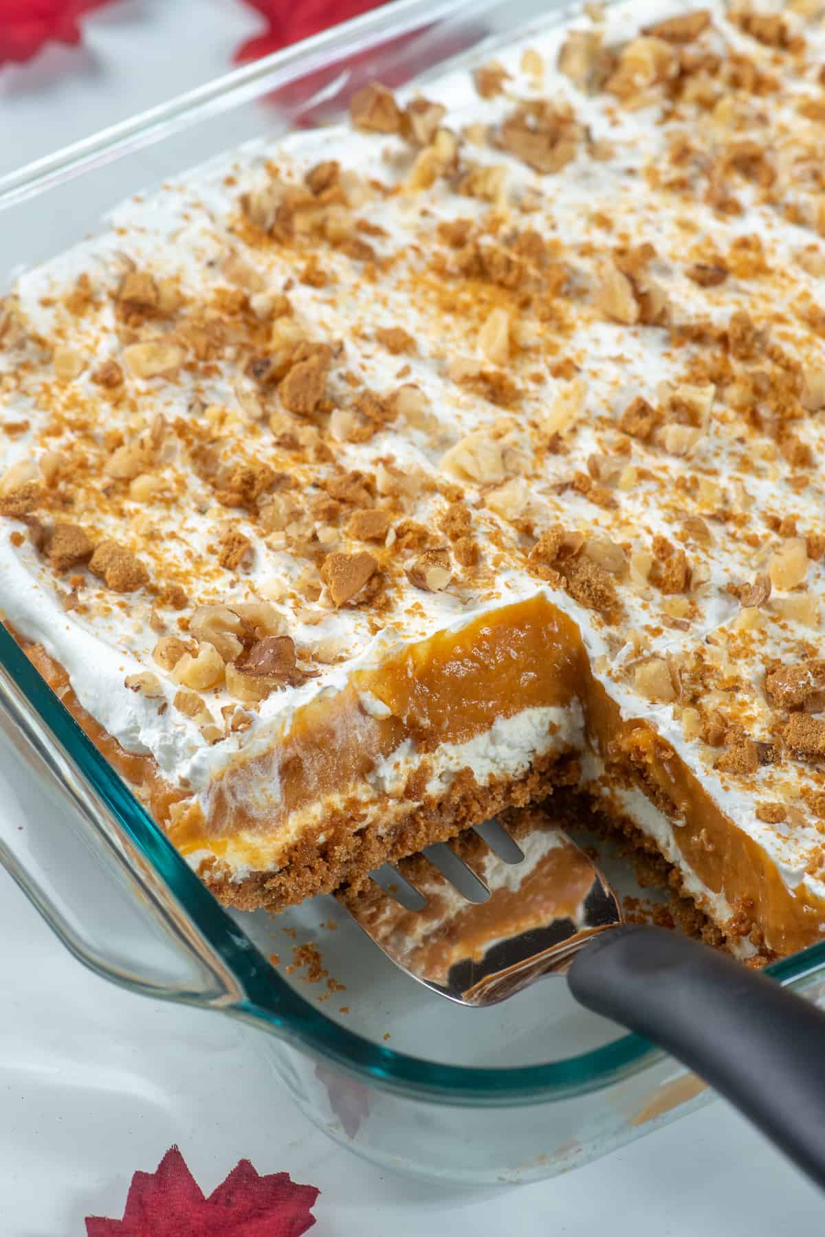 A spatula resting in a glass dish filled with layered pumpkin dessert.