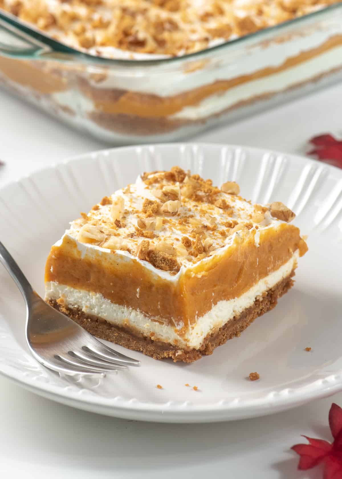 A slice of layered pumpkin dessert on a white plate with a fork.