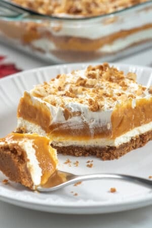 A slice of layered pumpkin dessert on a white plate with a fork.