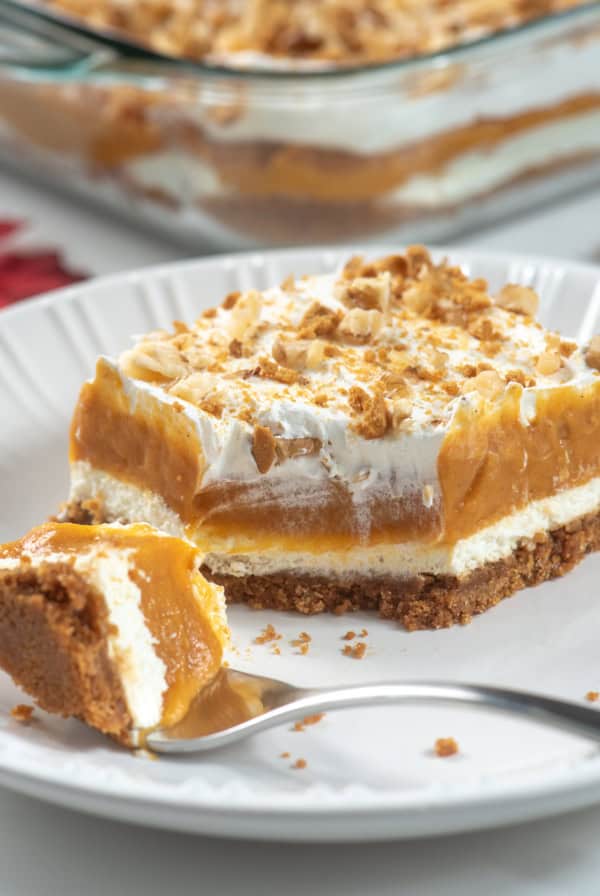 A slice of layered pumpkin dessert on a white plate with a fork.