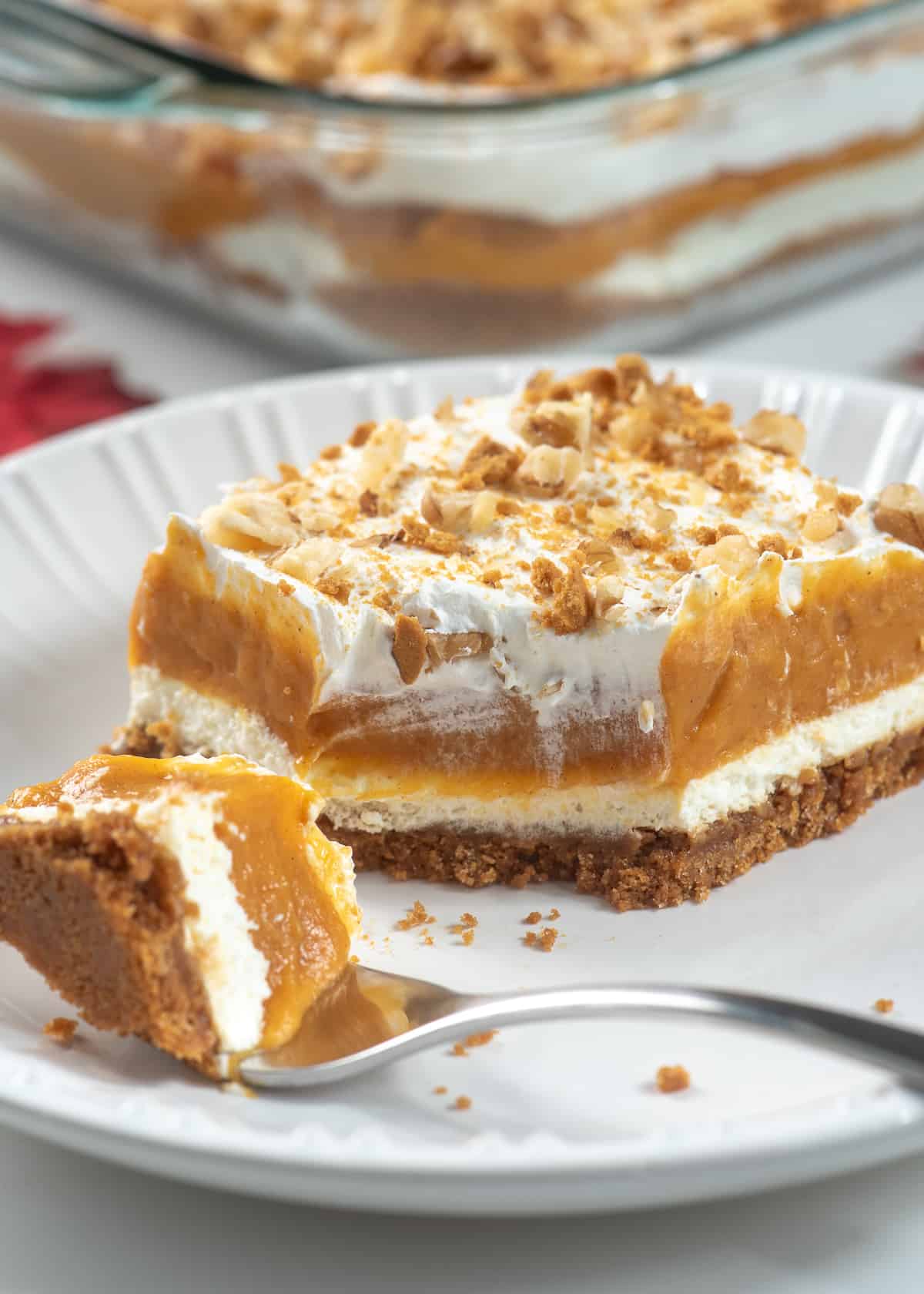 A slice of layered pumpkin dessert on a white plate with a fork.