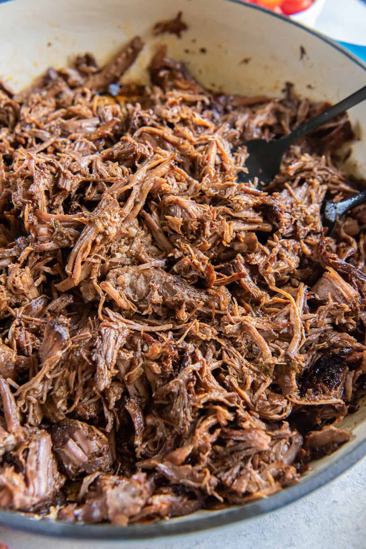 A close up of two forks resting in a pan full of shredded beef.