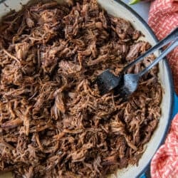 A top down shot of two forks resting in a pan full of Mexican shredded beef surrounded by bowls of taco toppings.