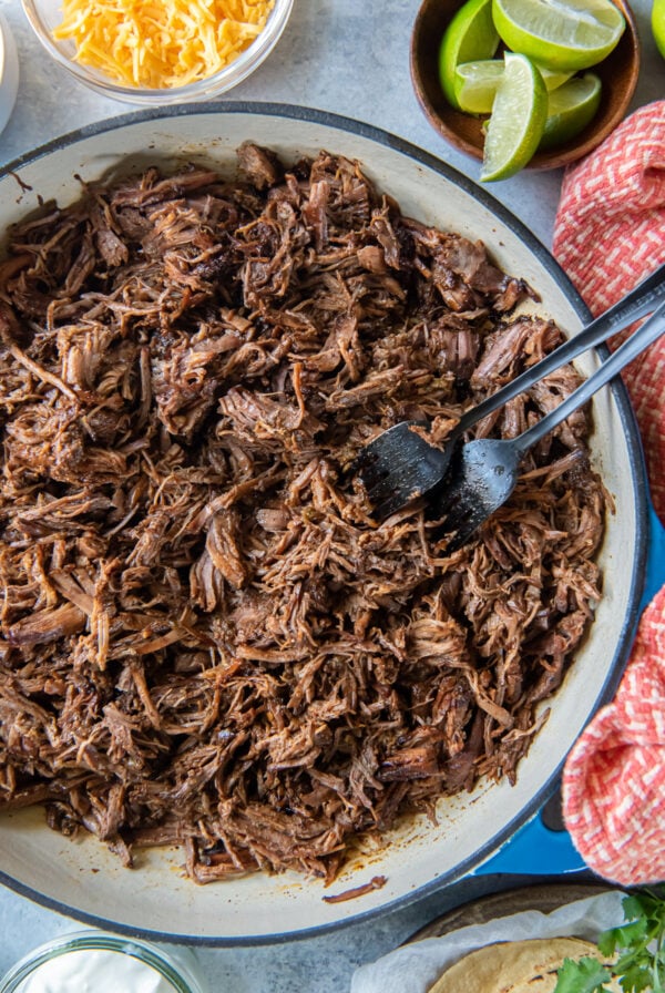 Two forks resting in a pan of Mexican shredded beef.