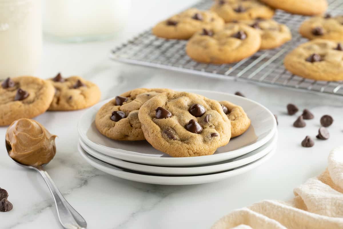 Three peanut butter chocolate chip cookies on a stack of white plates.