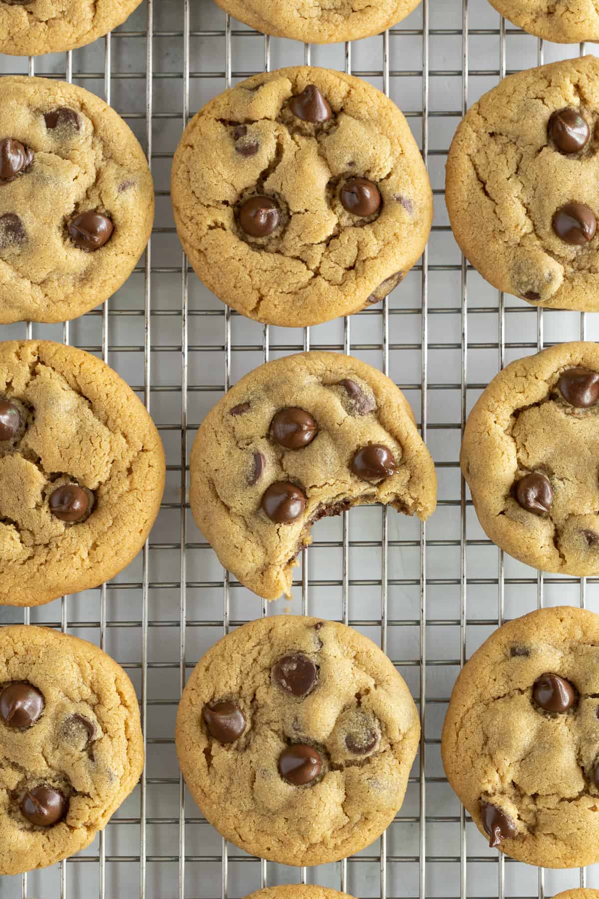 A top down shot of peanut butter cookies with chocolate chips on a wire rack with a bite missing from one.