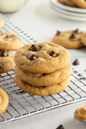 A stack of three peanut butter chocolate chip cookies on a wire rack.