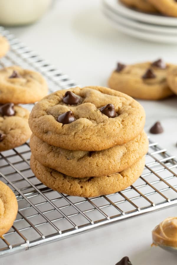 A stack of three peanut butter chocolate chip cookies on a wire rack.