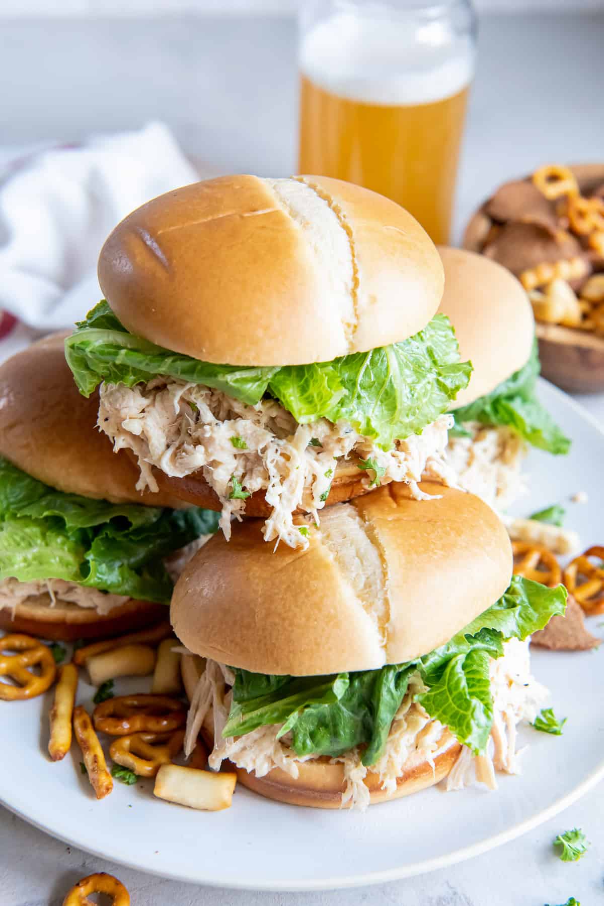 A chicken caesar sandwich on a bun with lettuce stacked on top of two others with a glass of beer in the background.