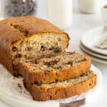 A partially sliced loaf of chocolate chip banana bread on a white platter.