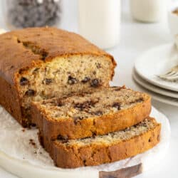 A partially sliced loaf of chocolate chip banana bread on a white platter.