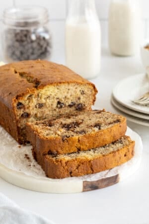 A partially sliced loaf of chocolate chip banana bread on a white platter.