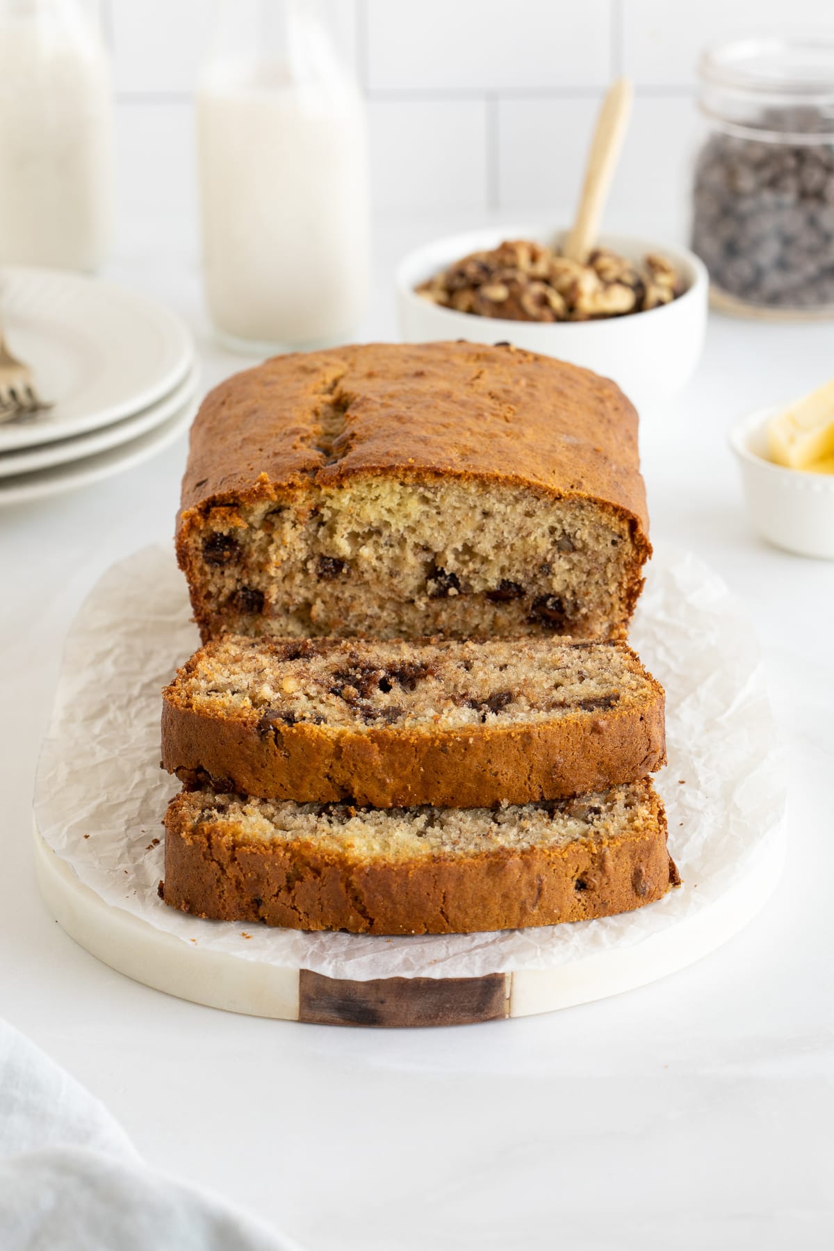 A partially sliced loaf of banana bread with chocolate chips on a white platter.