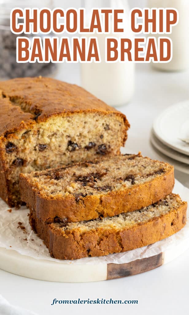 A partially sliced loaf of chocolate chip banana bread on a white platter with text.