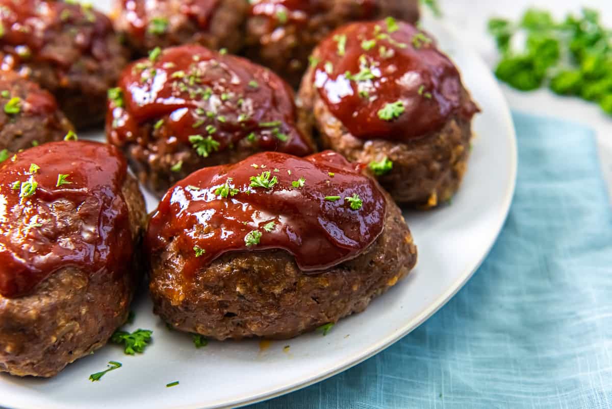 A close up of individual mini meatloaves with glaze on a white platter.