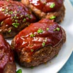 A close up of individual mini meatloaves with glaze on a white platter.