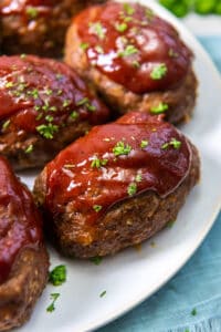 A close up of individual mini meatloaves with glaze on a white platter.