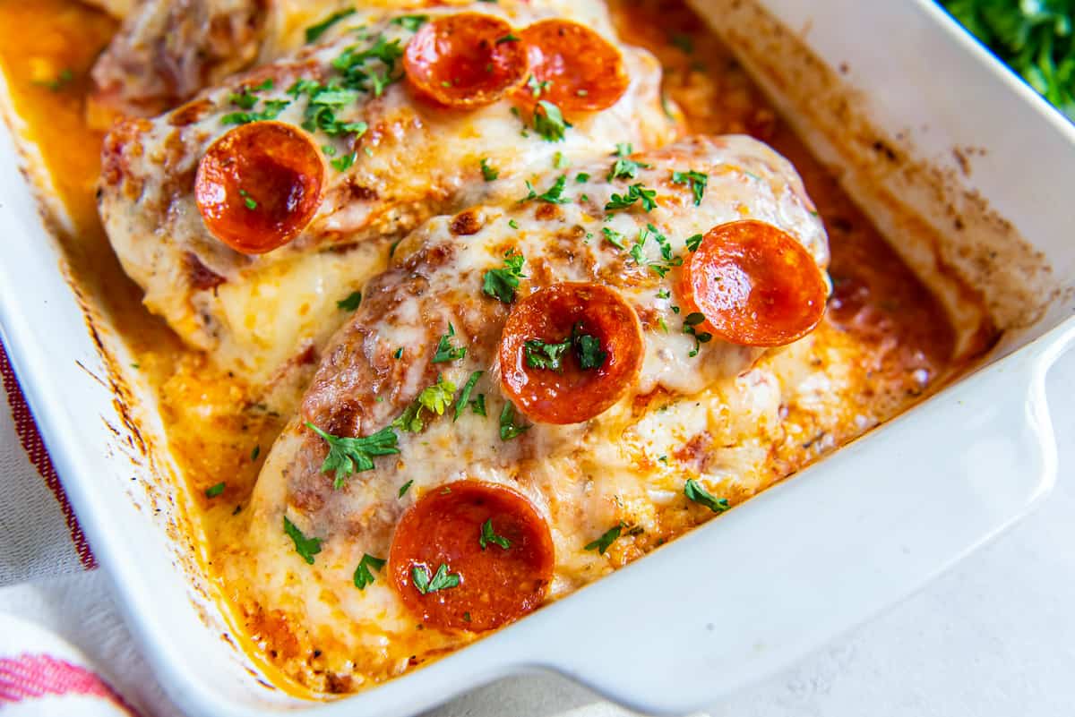 A close up of stuffed pizza chicken topped with slices of pepperoni in a baking dish.