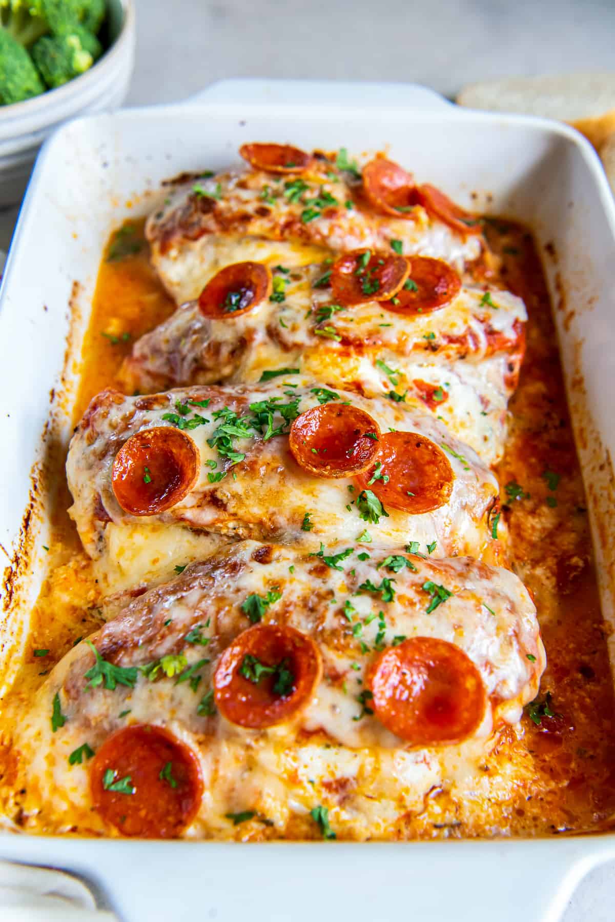 A side view of four pieces of stuffed chicken topped with cheese and pepperoni in a baking dish.