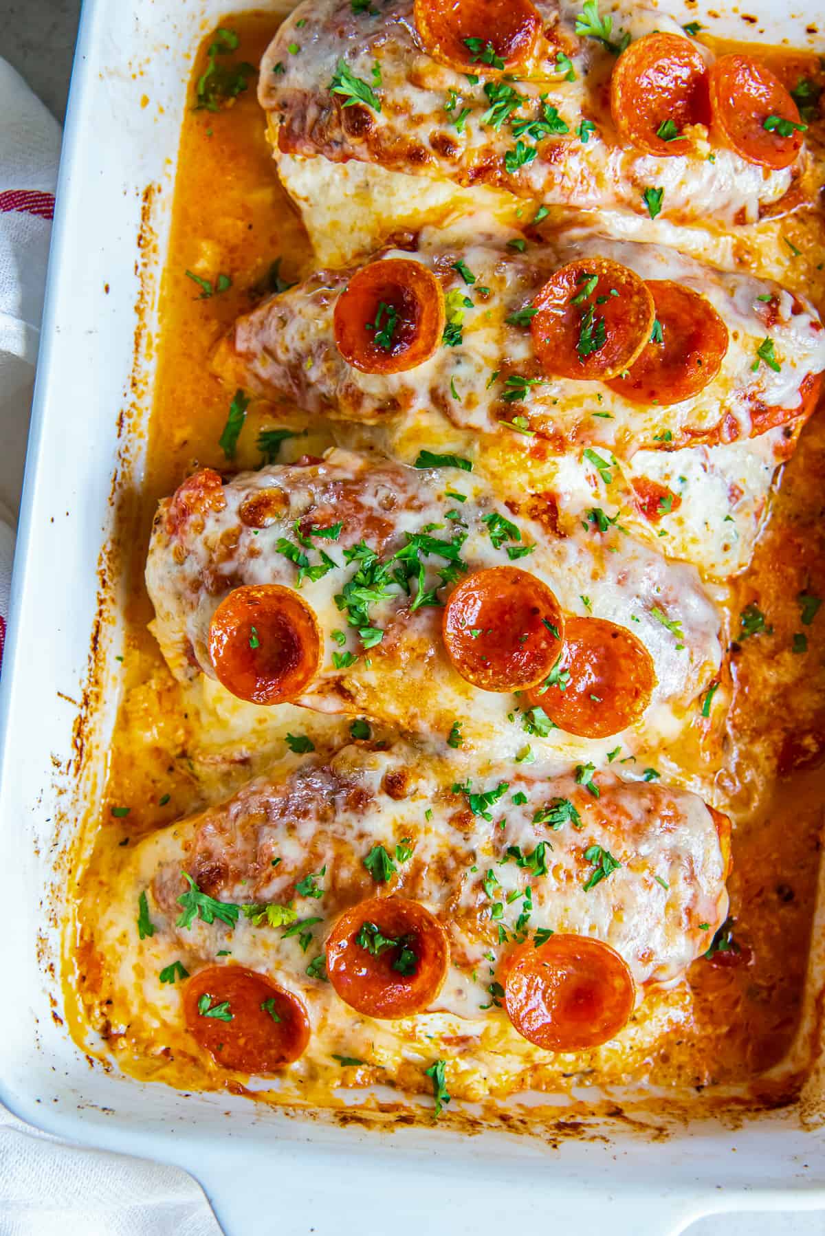 A top down shot of four pieces of stuffed chicken topped with cheese and pepperoni in a baking dish.