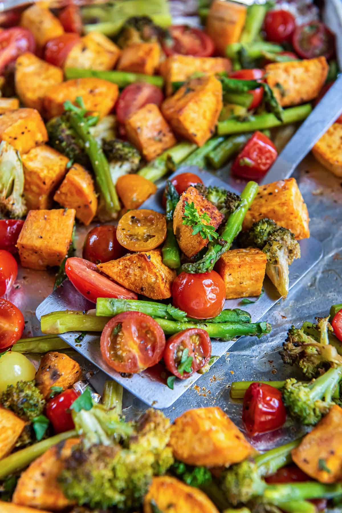 A spatula scooping roasted vegetable from a sheet pan.