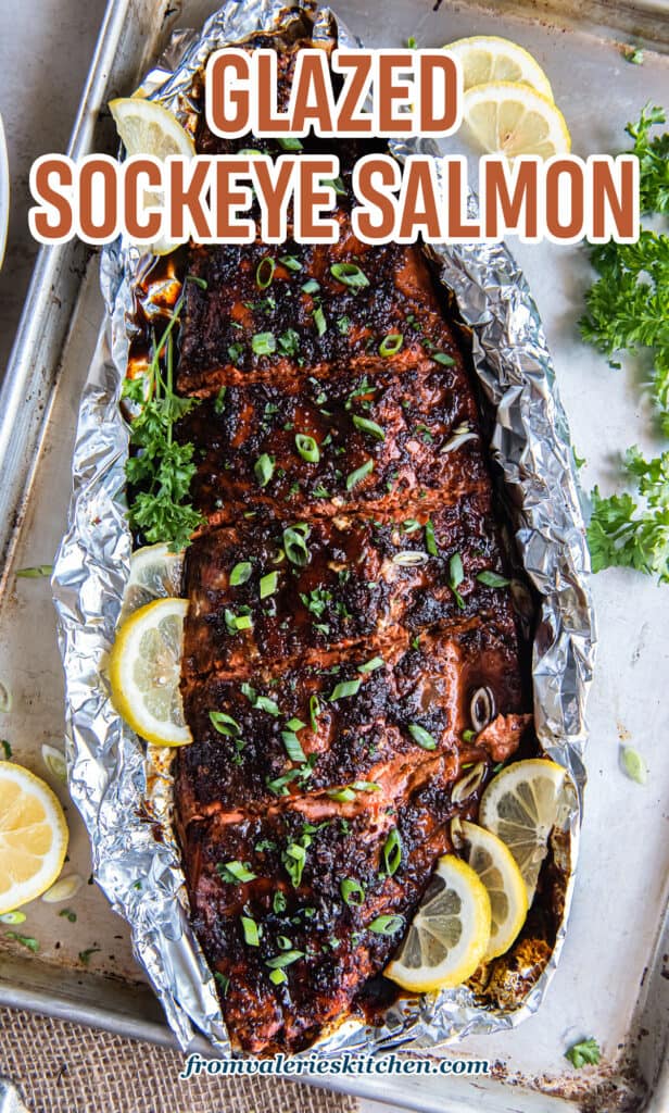 A top down shot of a glazed sockeye salmon fillet garnished with green onions and lemon slice on a sheet of foil with text.