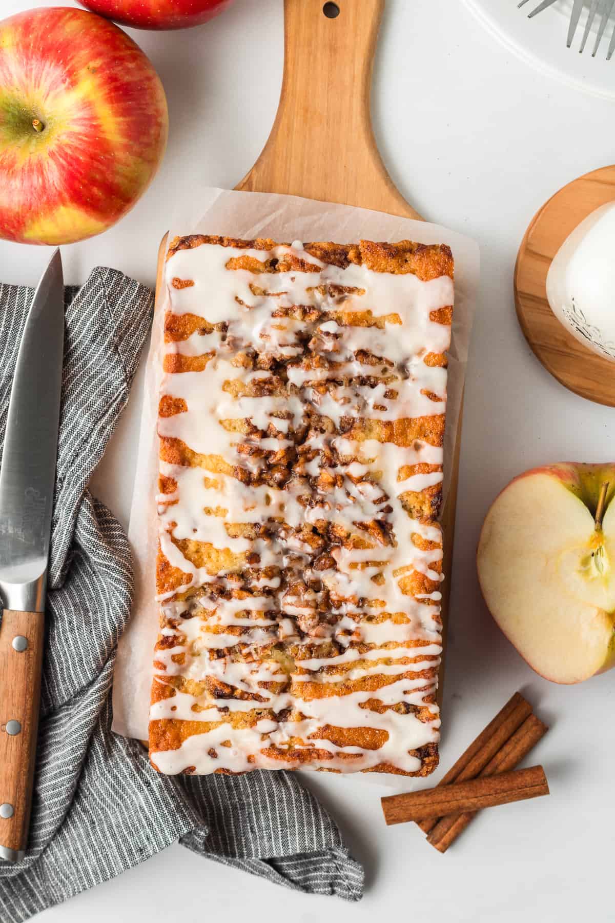 A top down shot of a loaf of apple fritter bread with glaze on a wood board.