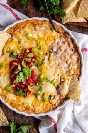 A top down shot of a tortilla chip pressed into bean dip topped with melted cheese, salsa, and green onions.