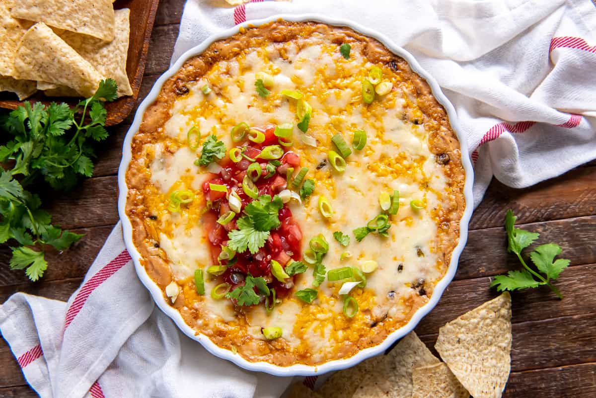 A top down shot of cheesy bean dip topped with salsa and green onions in a white baking dish.