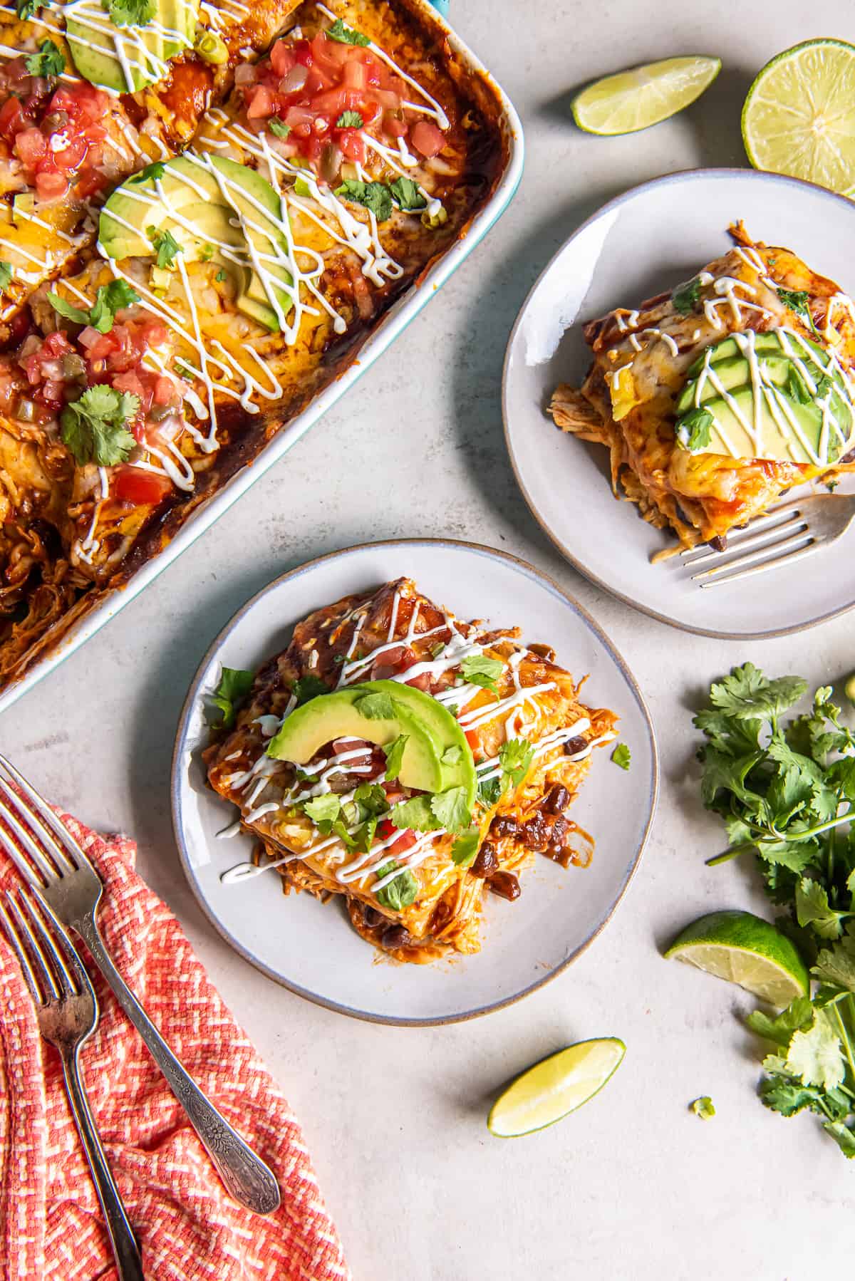 Two servings of chicken enchilada casserole on white plates with the casserole next to them.