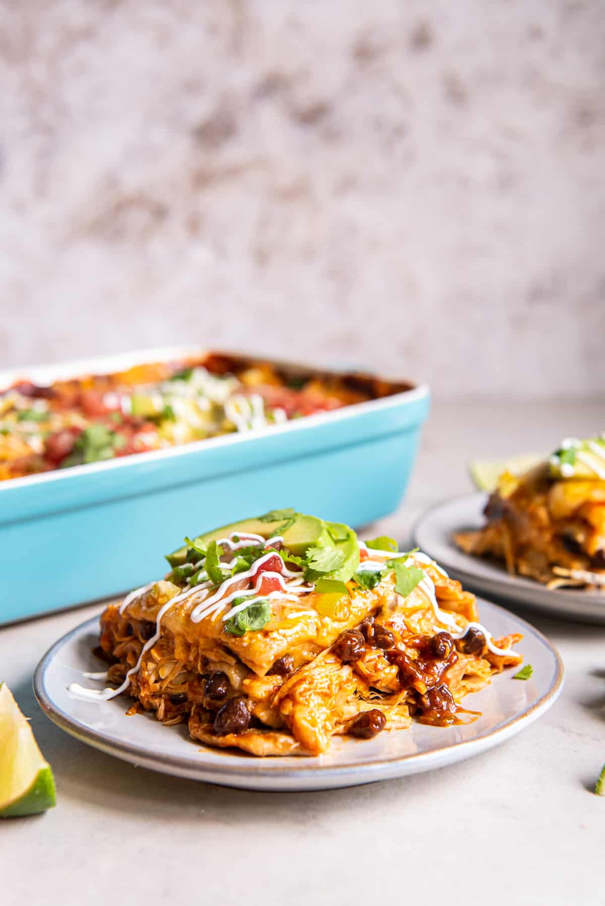 A serving of chicken enchilada casserole on a white plate with a blue casserole dish in the background.