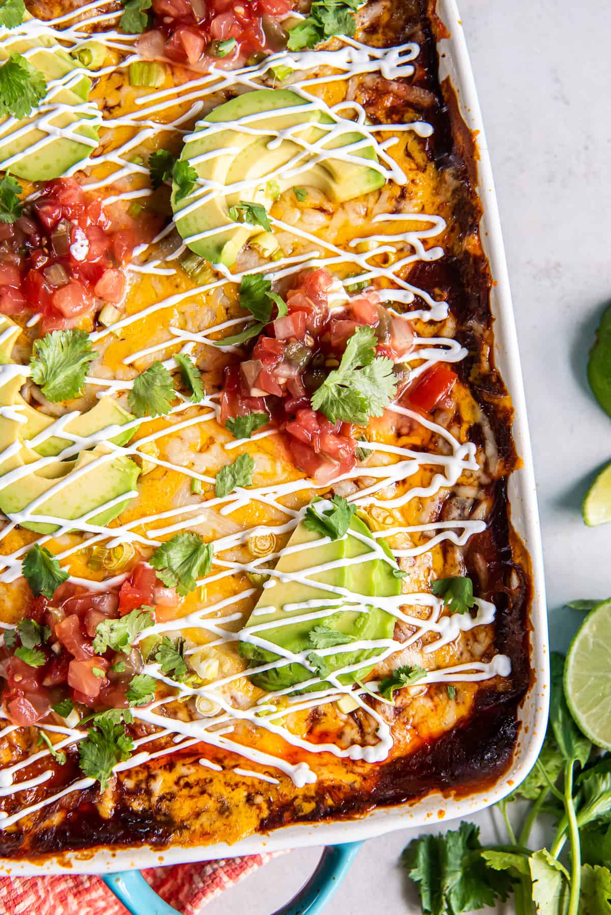 A top down closeup shot of chicken enchilada casserole topped with sour cream and sliced avocado.