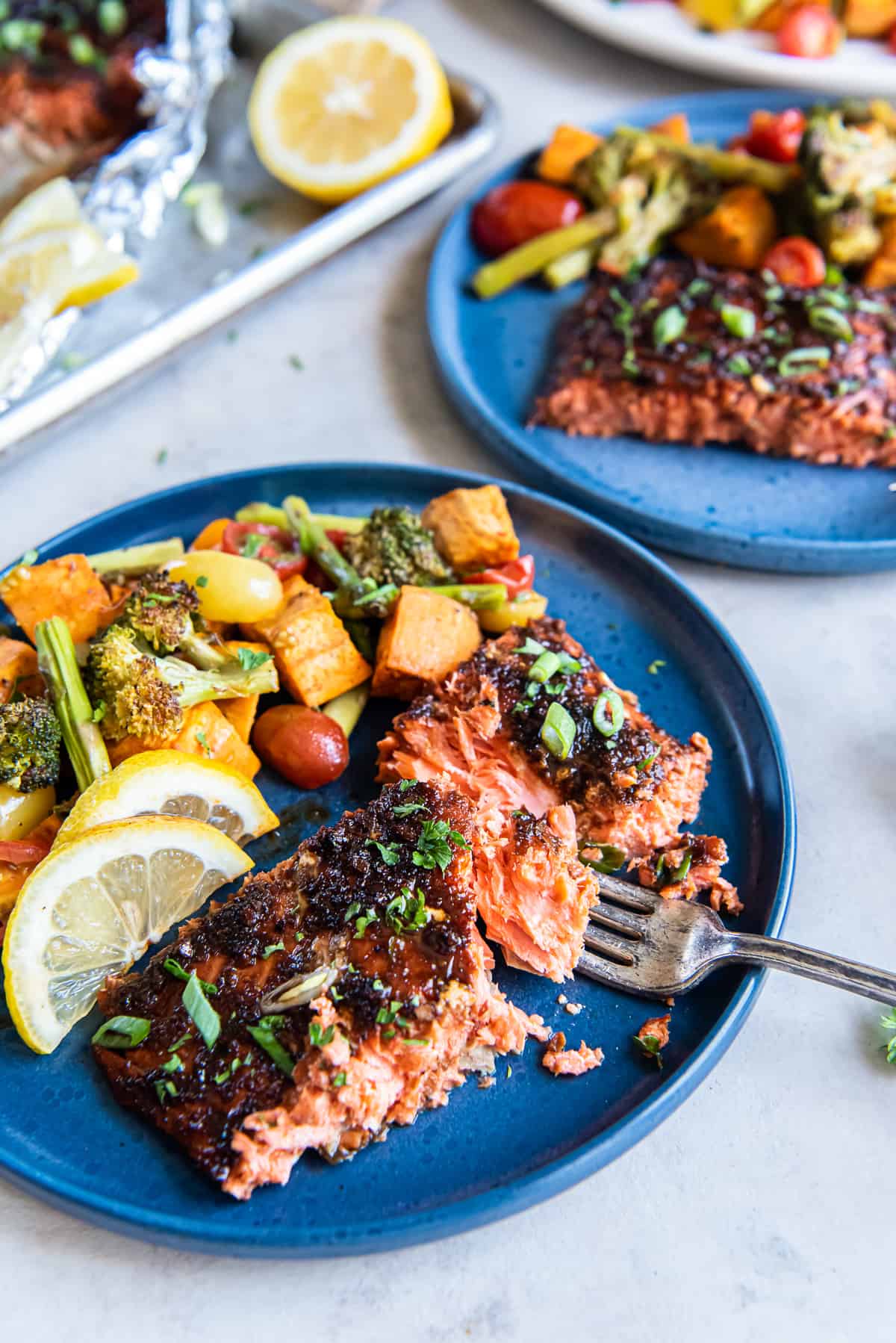 A fork breaking into a slice of glazed sockeye salmon on a blue plate with roasted vegetables.