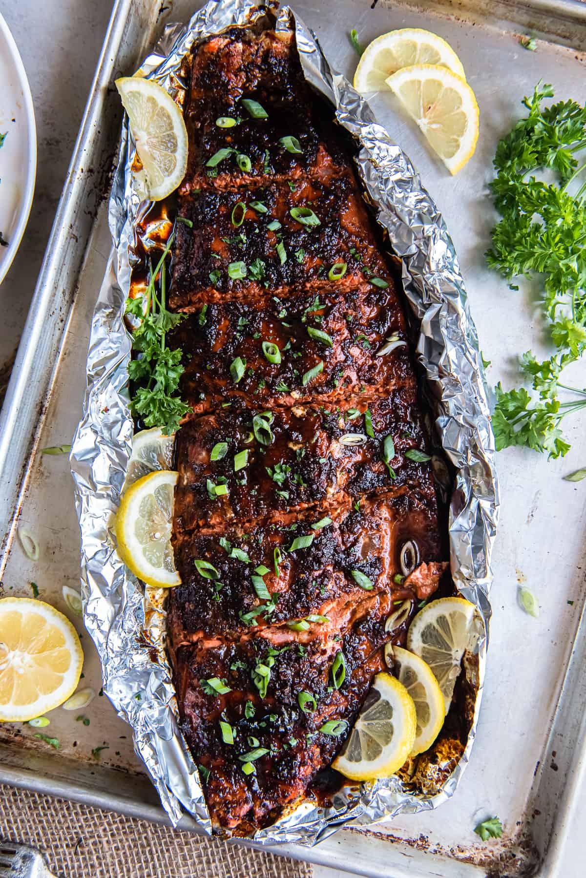 A top down shot of a glazed sockeye salmon fillet on foil with lemon slices.