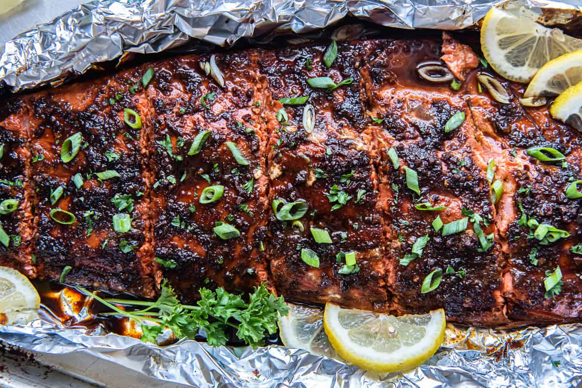 A close up top down shot of a glazed sockeye salmon fillet on foil with lemon slices.