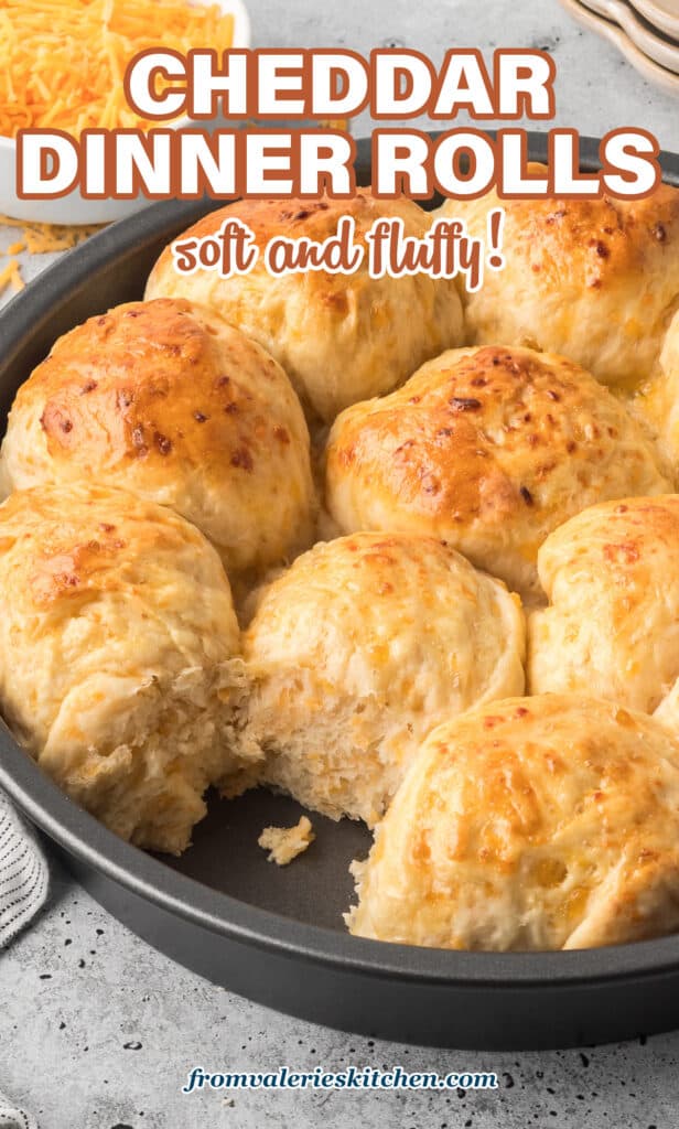 A metal cake pan filled with cheddar rolls with one missing with text.