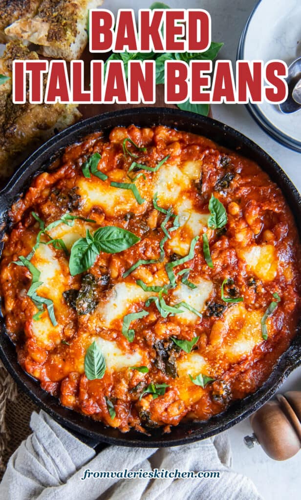 Cannellinni beans in marinara sauce with kale and cheese in a cast iron skillet next to pieces of foccacia bread and fresh basil with text.