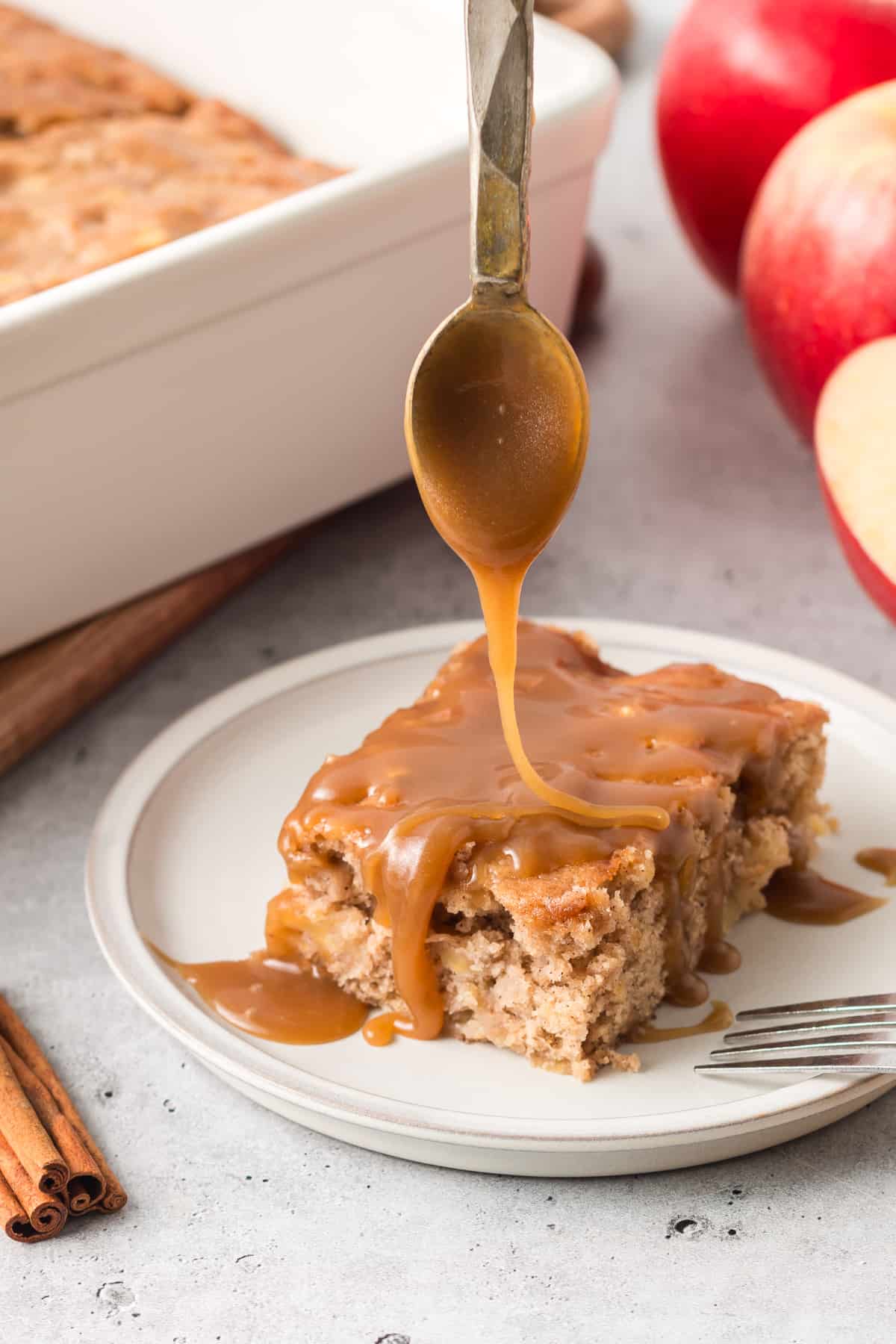 Butterscotch sauce drizzling off the end of a spoon and on to a slice of apple cake on a plate.