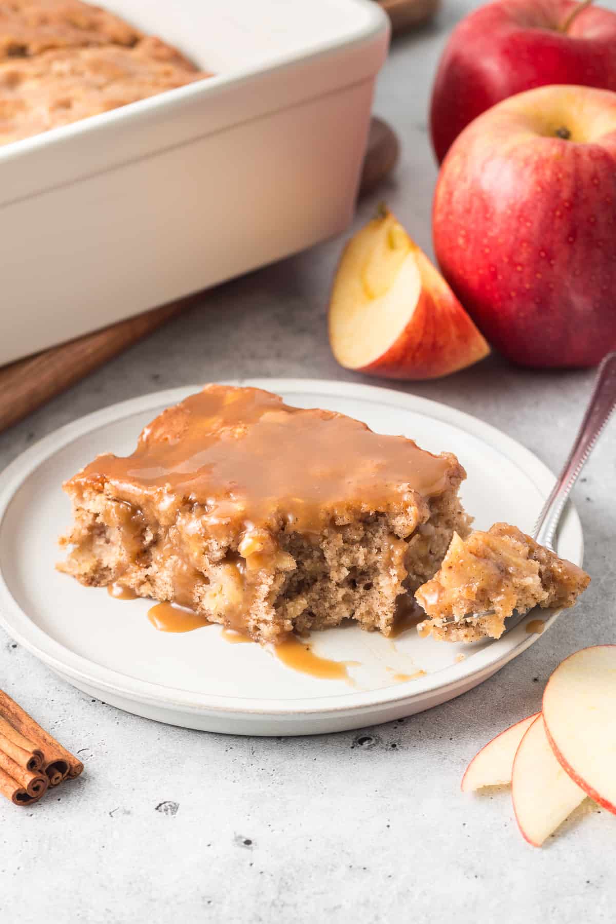 A slice of apple cake with butterscotch sauce on a white plate with a fork.